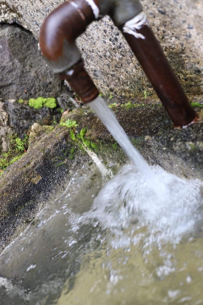 A rustic water tap pouring clear water into a moss-covered stone basin at the campsite.