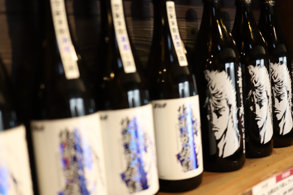 Bottles of Mitsutake sake featuring special collaboration labels with the manga series Fist of the North Star (Hokuto no Ken), displayed at Mitsutake Brewery in Kashima, Saga.