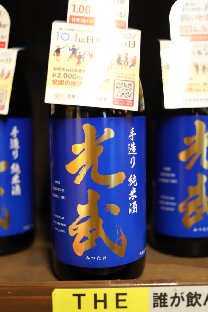 A bottle of Mitsutake hand-crafted Junmai sake with a vivid blue label on display at Mitsutake Sake Brewery in Kashima, Saga.