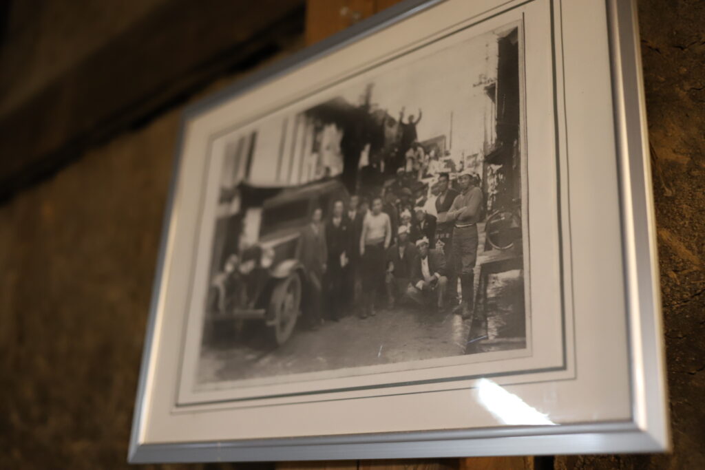 Framed black-and-white photo of brewery workers and townspeople in front of a car, displayed at Mitsutake Sake Brewery in Kashima, Saga.