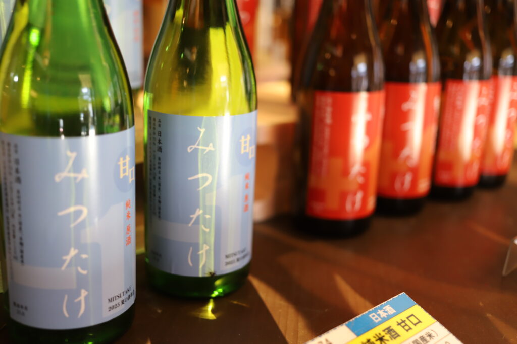 Bottles of Mitsutake sake with light blue labels displayed at the brewery shop in Kashima, Saga.