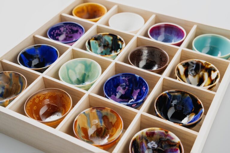 Colorful Arita porcelain sake cups by Sin'emon kiln, neatly arranged in a wooden box. Each cup features unique glazing and patterns, showcasing the fusion of tradition and innovation in Japanese porcelain.